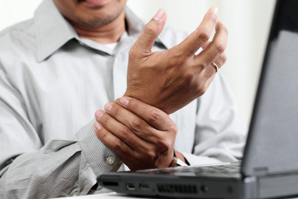 man with carpal tunnel syndrome holding hurt wrist sitting at laptop