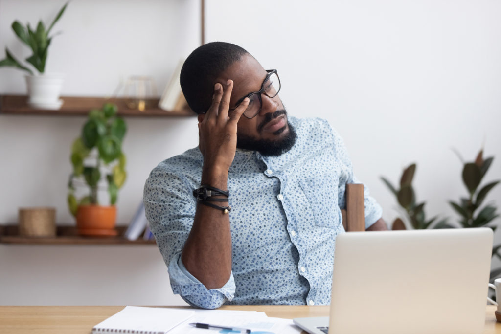 A Black man sits in deep thought at his computer - how to choose the best L&I attorney.
