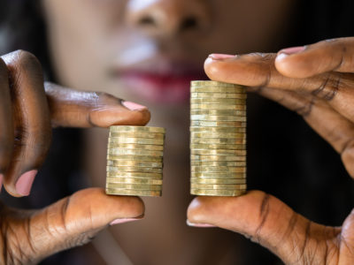 Black woman holds two unequal stacks of gold coins in her fingers to illustrate wage gap - Equal Pay Employment Attorneys Emery Reddy