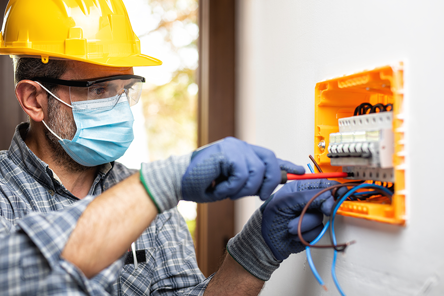 Electrician at work on an electrical panel protected by helmet, safety goggles and gloves as personal protective equipment