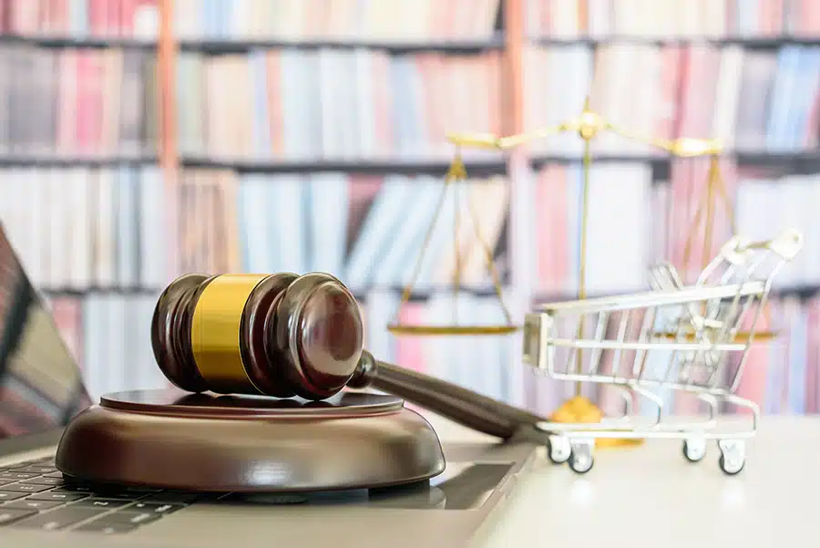 A gavel rests on its side with a legal bookshelf behind it.