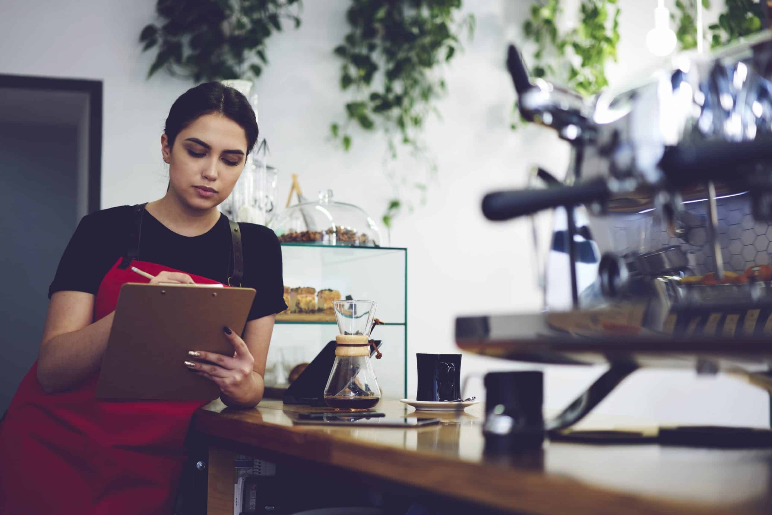 barista taking inventory leaning up against a counter with baked goods in the background
