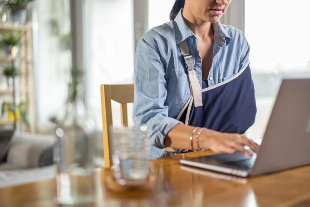 Woman working on laptop with an arm in a sling