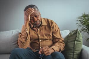 An adult has a headache. He sits and holds his hands on his head in a dark room. Concept of dramatic loneliness, sadness, depression, sad emotions, disappointment, nursing, pain.