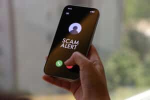 A person holds a smartphone displaying a “Scam Alert” message on an incoming call screen. The dark interface clearly indicates a fraud warning, conveying concerns about cybersecurity, mobile fraud, and digital safety. The indoor environment and close-up composition highlight the immediacy and relevance of online threat awareness in everyday mobile use.
