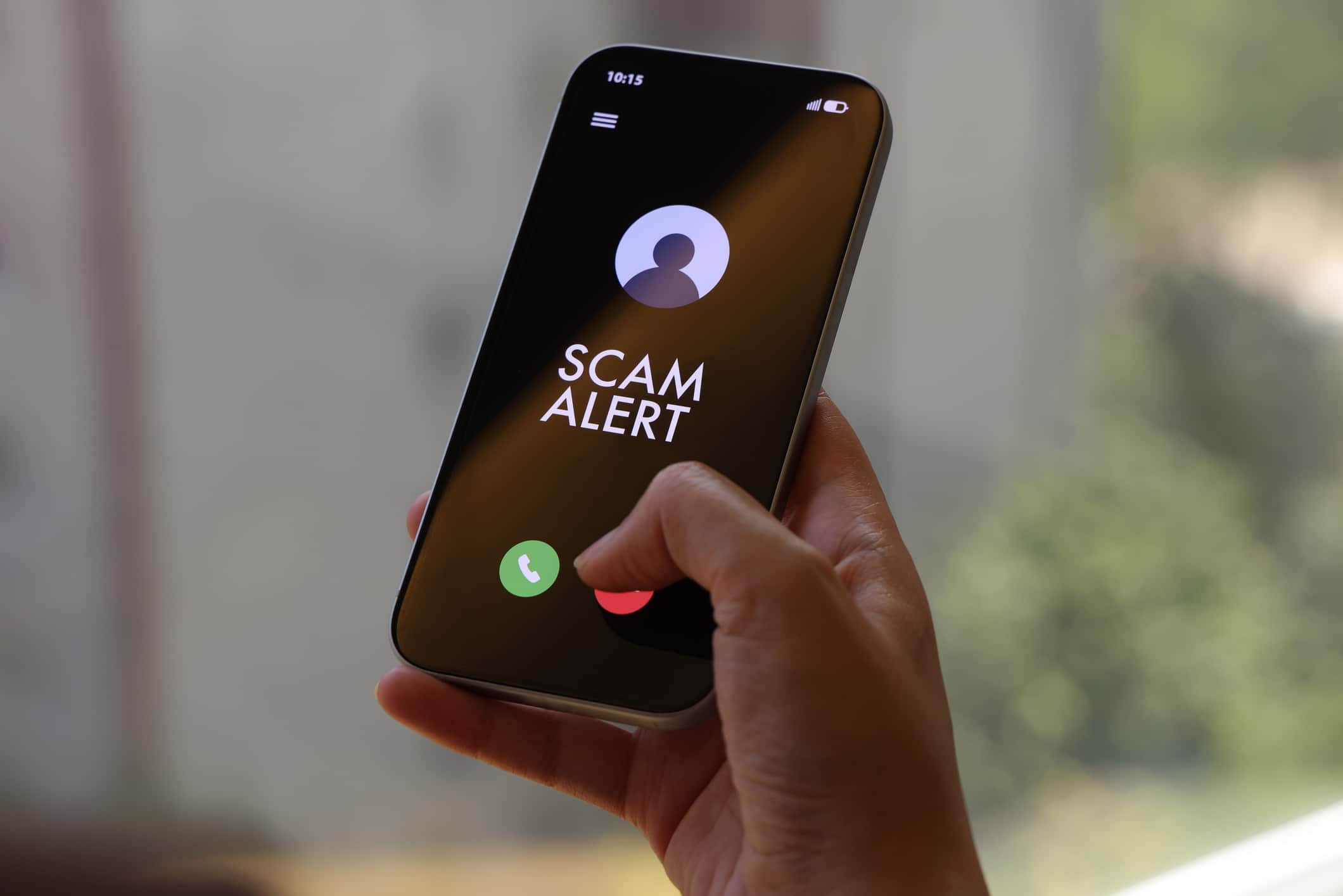 A person holds a smartphone displaying a “Scam Alert” message on an incoming call screen. The dark interface clearly indicates a fraud warning, conveying concerns about cybersecurity, mobile fraud, and digital safety. The indoor environment and close-up composition highlight the immediacy and relevance of online threat awareness in everyday mobile use.