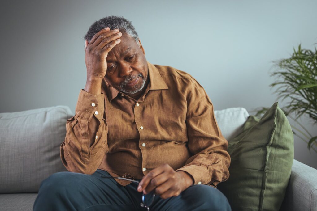 An adult has a headache. He sits and holds his hands on his head in a dark room. Concept of dramatic loneliness, sadness, depression, sad emotions, disappointment, nursing, pain.